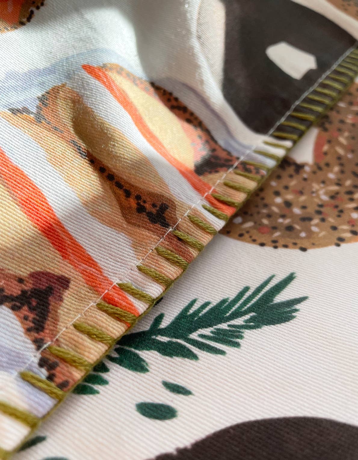 Close up of details on bagel tea towel. Shows the green, embroidered stitching along the edges. 