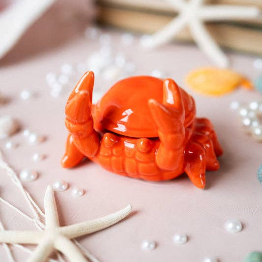 Orange ceramic crab on a decorative surface with starfish and pearls