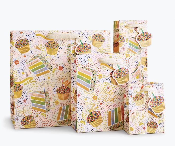 Birthday Cake Gift Bag shown in multiple sizes.  Illustration on bag features cupcakes and slices of colorful layer cake with lots of sprinkles. Multiple areas of text read "Make a WIsh!" and "Wishing you a very Happy Birthday" in gold script.