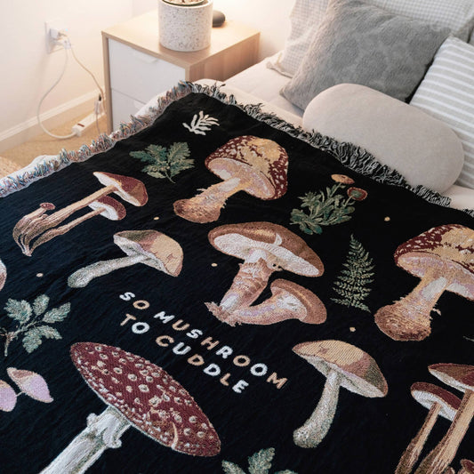 Mushroom throw blanket on bed -- blanket has text that reads "So Mushroom To Cuddle" 