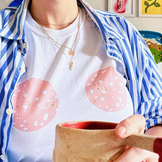 White t-shirt with two slices of mortadella in the middle, chest area. Shown on model wearing a striped overshirt, while drinking coffee.