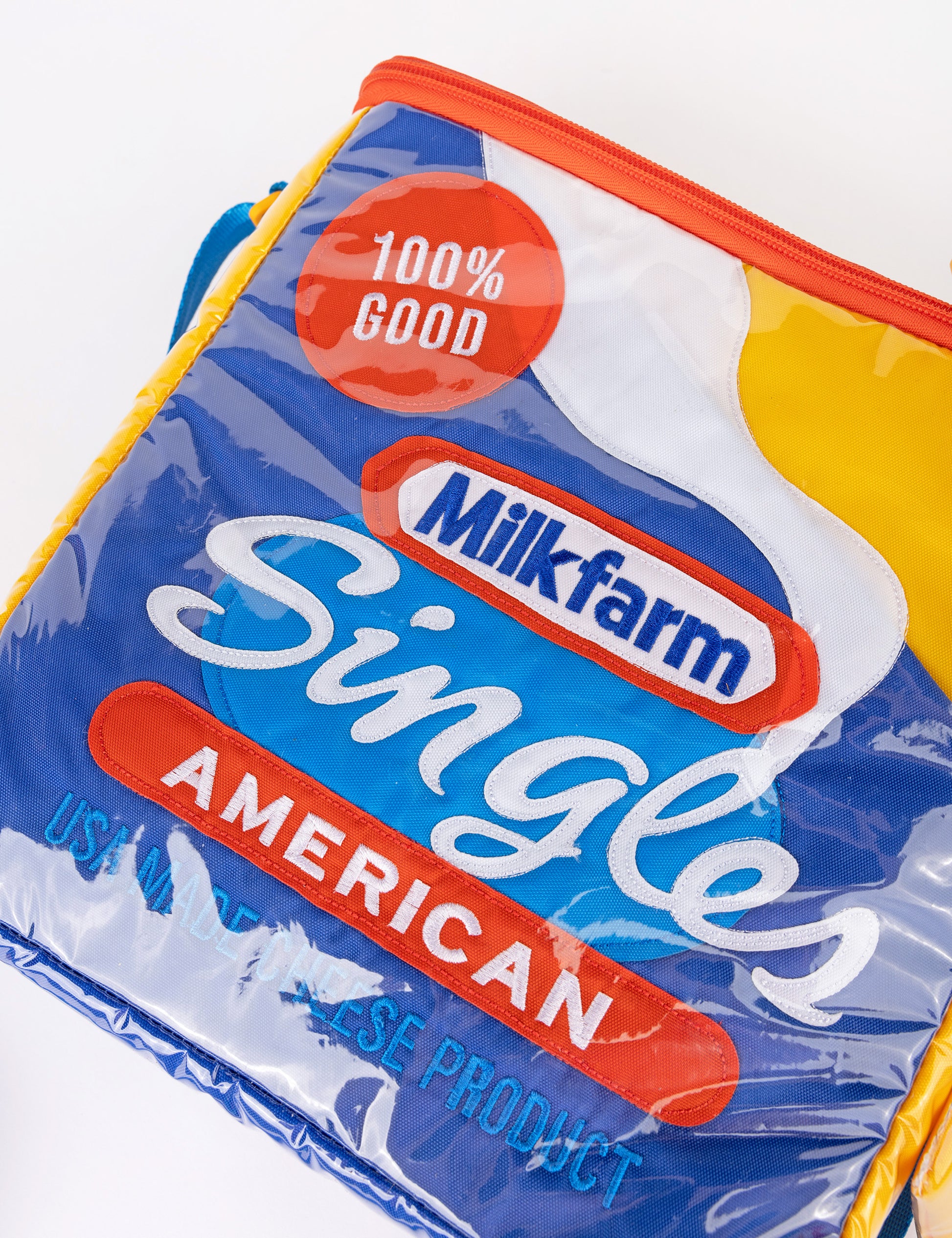 Milkfarm Singles Cheese Bag that looks like a Kraft Singles package. Multicolored with blue, white, red and mustard coloring. Text also says "100% Good/ American/ USA Made Cheese Product."