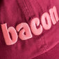 A close-up of a dark pink or magenta fabric surface with light pink embroidered letters spelling 'bacon' 