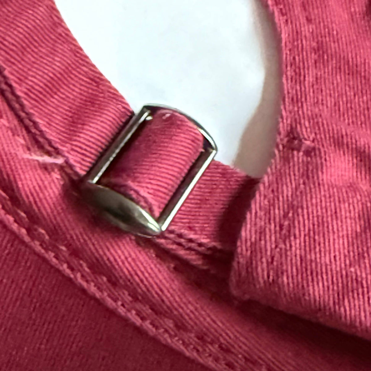 Close-up detail of a pink woven strap with a silver metal buckle on a garment.