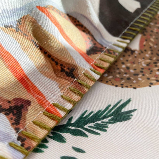 Close up of details on bagel tea towel. Shows the green, embroidered stitching along the edges. 