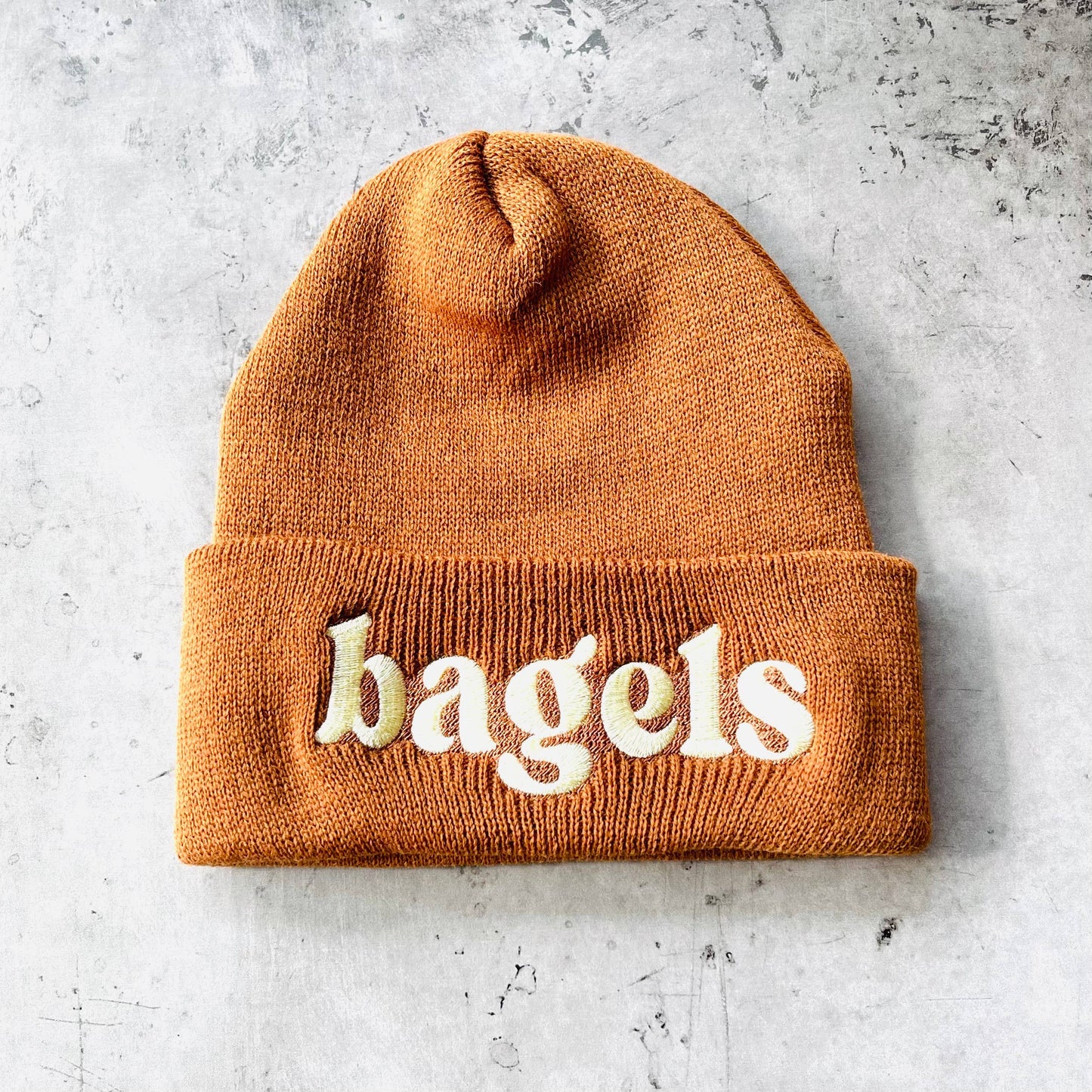 Brown beanie with white embroidery. Text simply reads: bagels