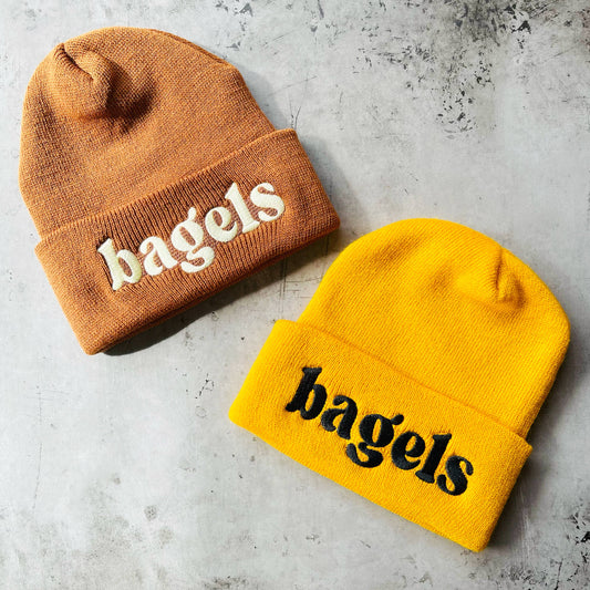 2 Beanies, one brown and one yellow. text on both of them reads: bagels