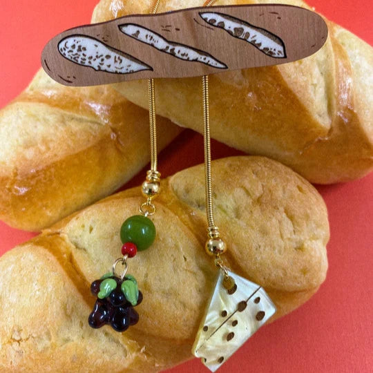 Bolo tie with a horizontal baguette as the main piece and smaller charms of olives, grapes and cheese below 