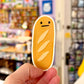 Hand holding a cartoon-style bread-shaped sticker with a store in the background