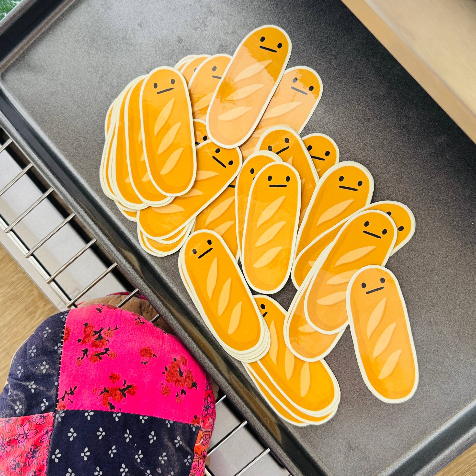 Yellow cartoonish baguette stickers on a baking tray with a colorful oven mitt.