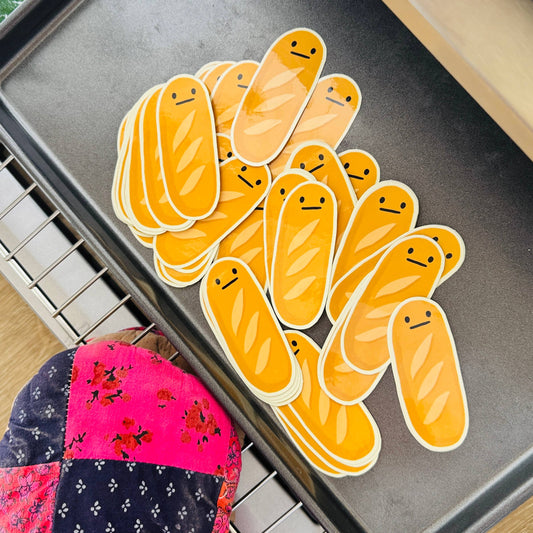 Yellow cartoonish baguette stickers on a baking tray with a colorful oven mitt.