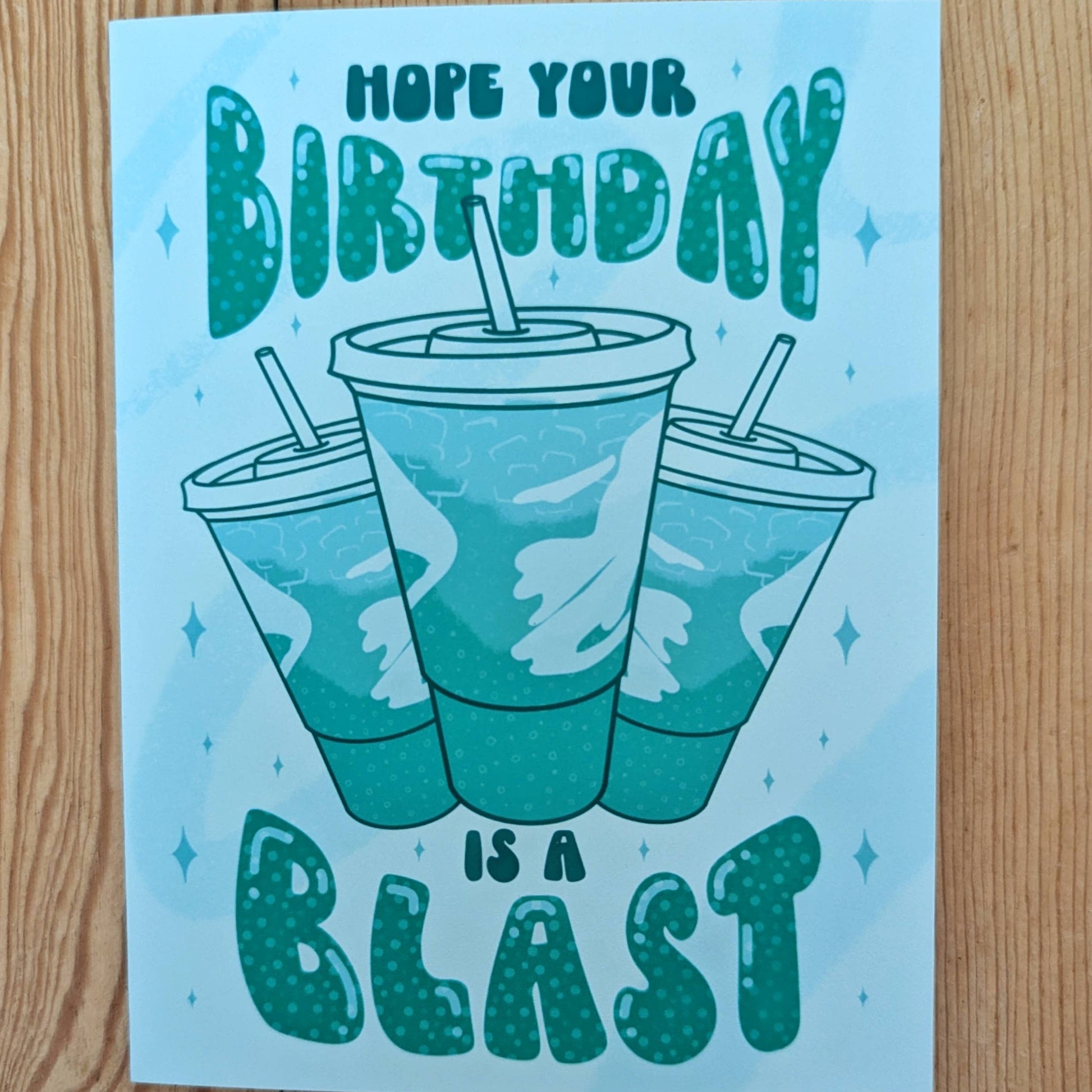 Greeting card with birthday message "hope your birthday is a blast" and soda cups of Baja Blast on a wooden surface