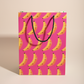 matte gift bag with grumpy face banana pattern on a pink background