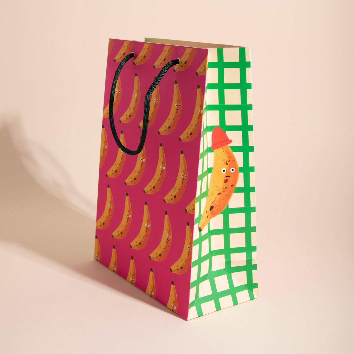 gift bag with grumpy face banana pattern on pink background. Side is on a white and green background