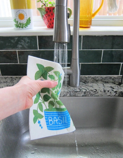 Photo of sponge cloth being squeezed under running water from a sink faucet.