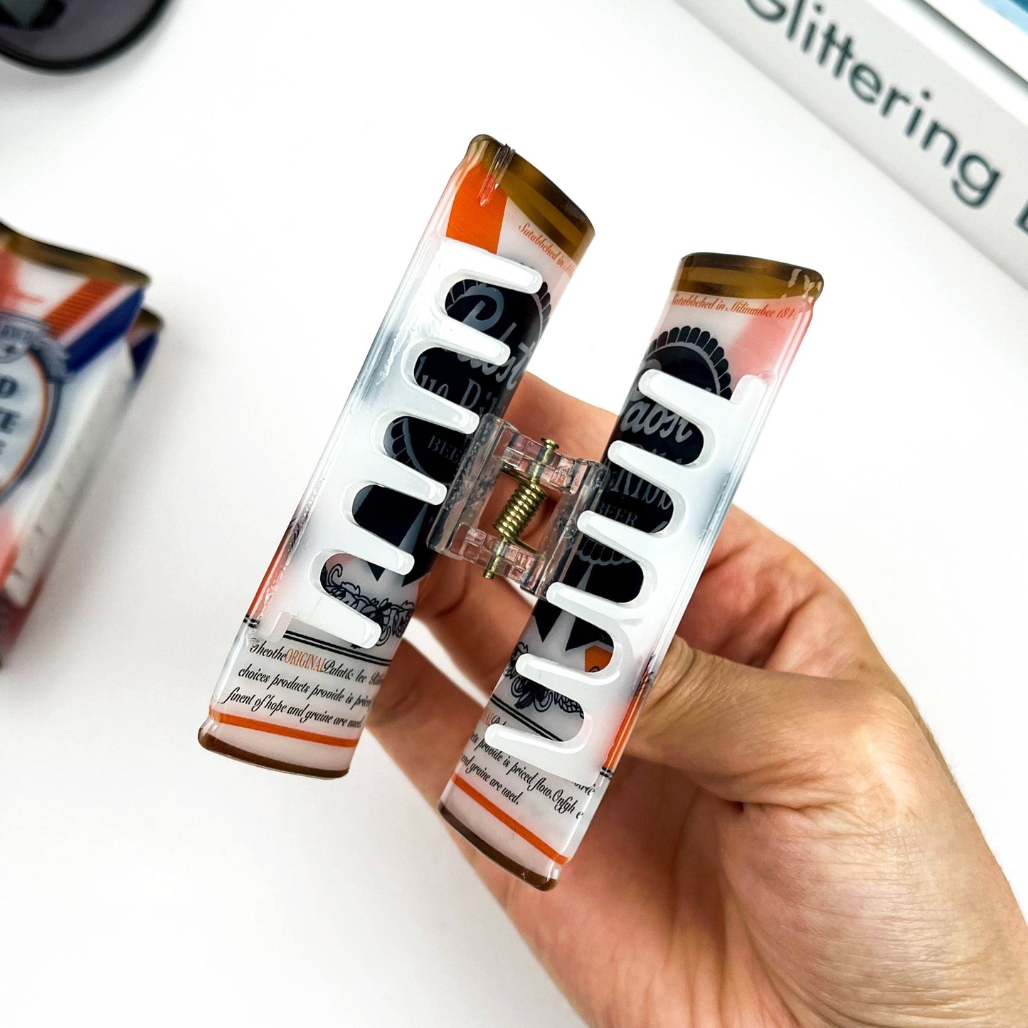 Hand holding a hair clipper with a clear design, surrounded by other similar products on a white surface.