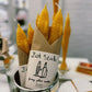 Set of two yellow beeswax taper candles shaped like fish. Shown in paper wrapping with "Fish Sticks" branding and logo.