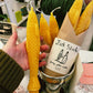Single yellow beeswax taper candle shaped like a fish. Shown unwrapped, resting in a person's open hand for scale.