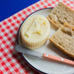 Candle that looks like a realistic piece of Beurre de Barrate. It is staged on a plate with a Sabre spreader and bread.
