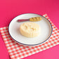 Candle that looks like a realistic piece of Beurre de Barrate. Staged on a plate with a butterknife that has a "baguette" handle.