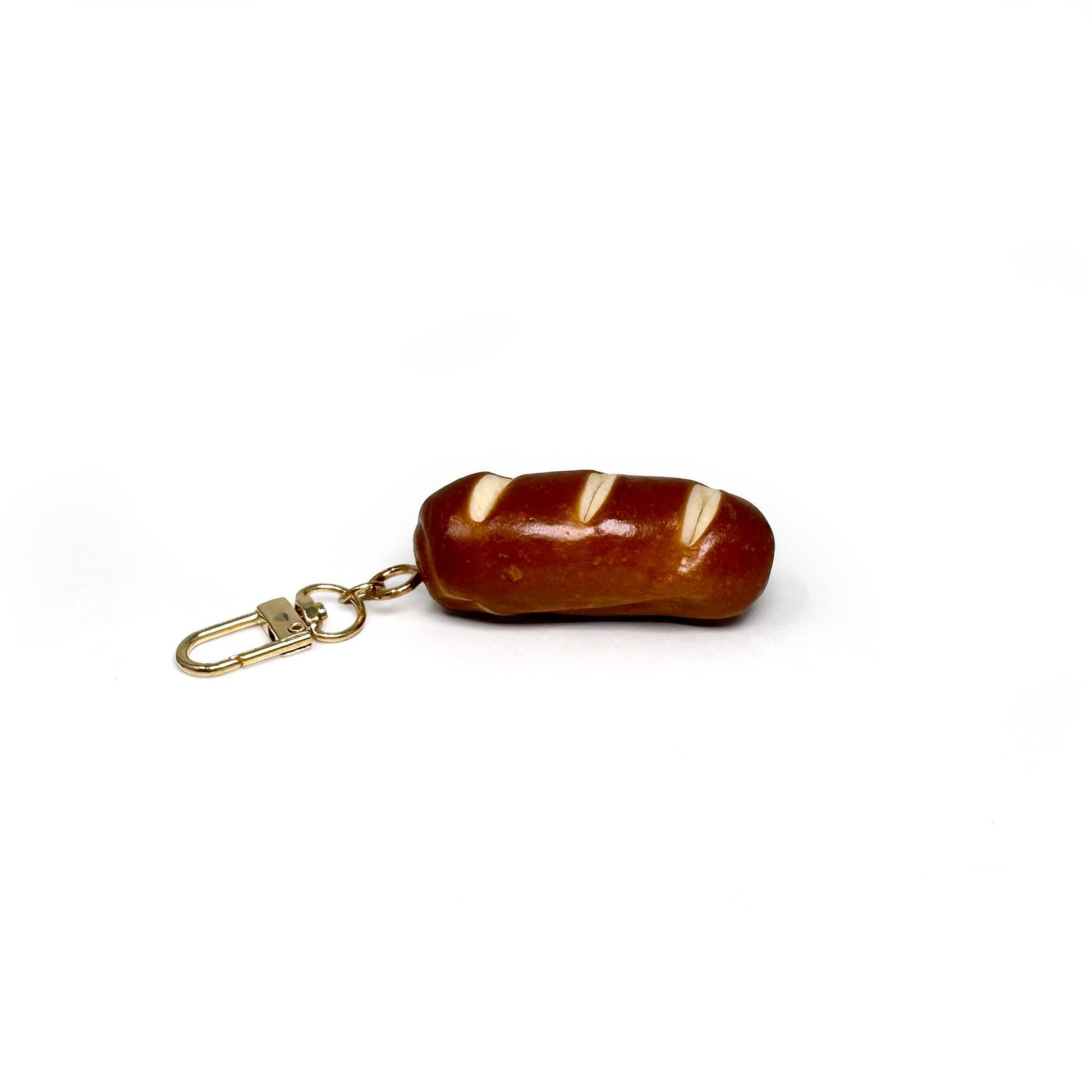 Keychain shaped like a realistic baguette (or pretzel roll) with toasty brown crust scored diagonally three times.