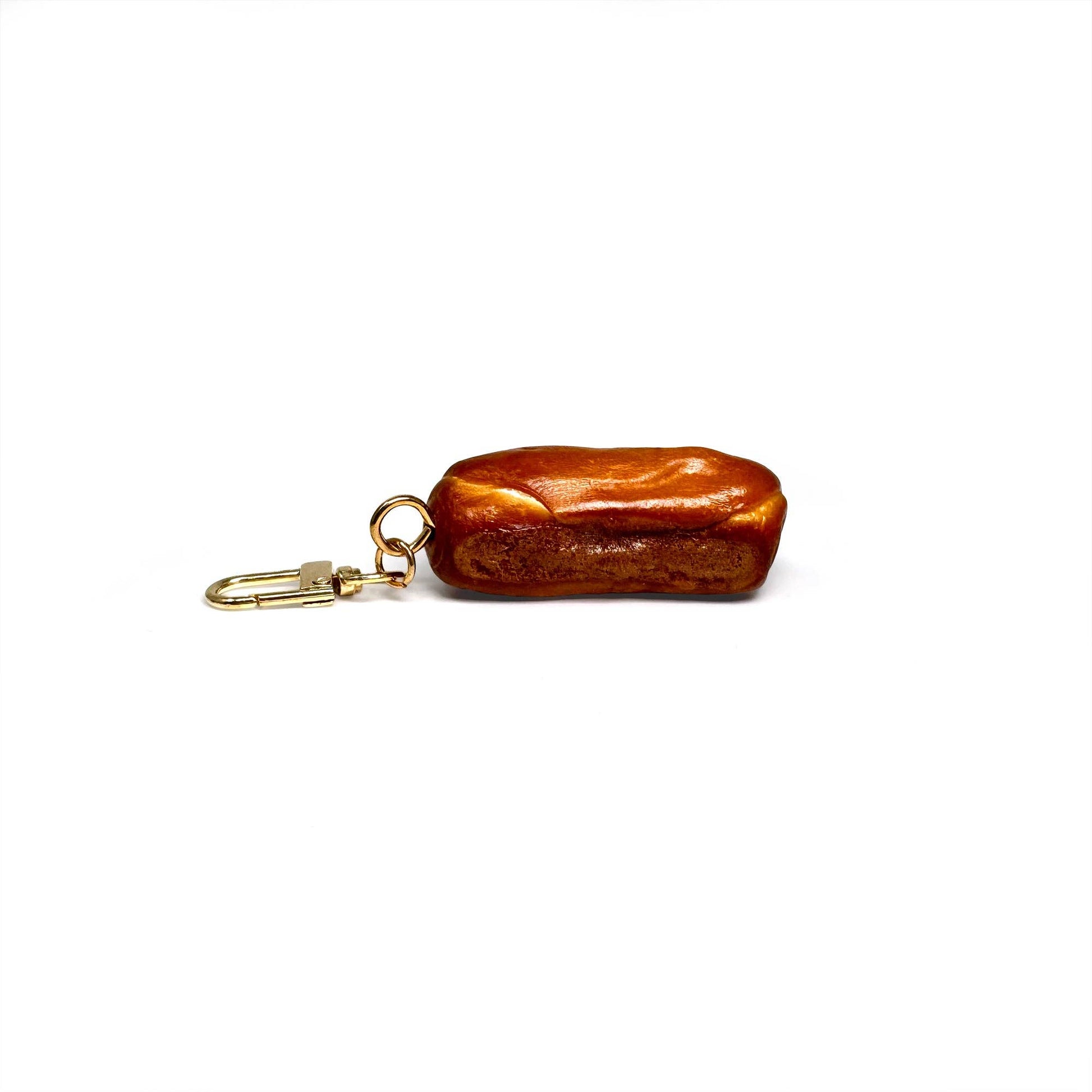 Keychain shaped like a realistic baguette (or pretzel roll) with toasty brown crust scored diagonally three times.
