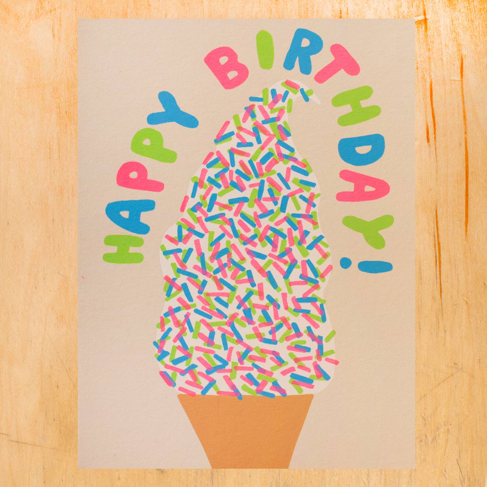 Birthday card with ice cream cone and colorful sprinkles on a wooden surface