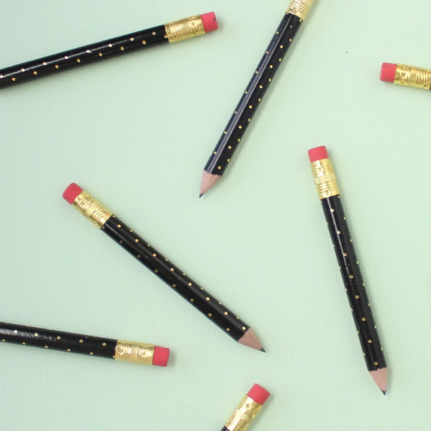 Mini black pencils with gold foil polka dots thrown on a green table.
