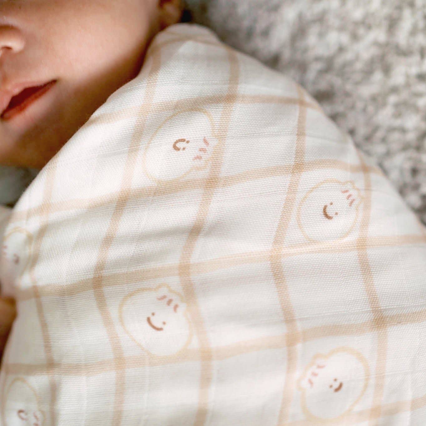 Close-up of a baby wrapped in a white blanket with smiley face patterns, lying on a textured surface.
