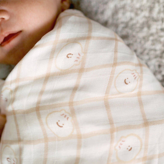 Close-up of a baby wrapped in a white blanket with smiley face patterns, lying on a textured surface.