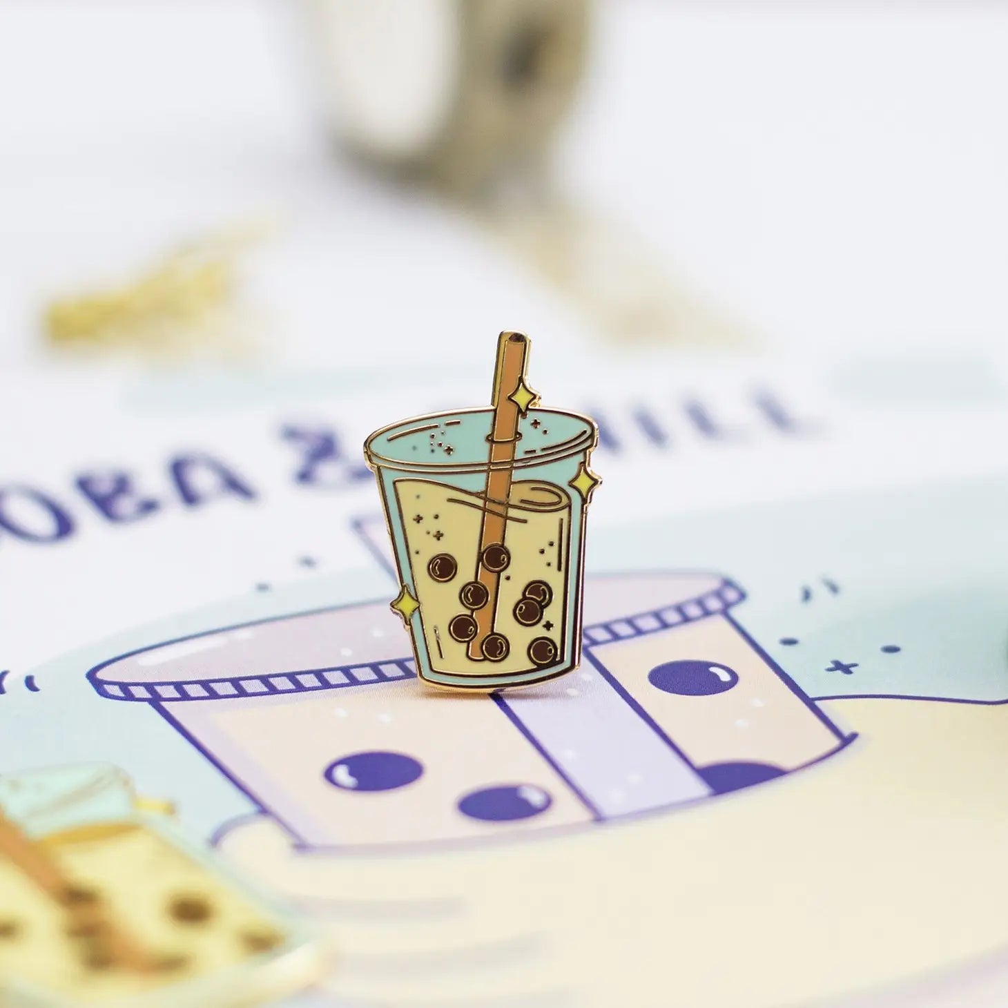 Close up of a boba lapel pin that has an orange straw and sparkles.