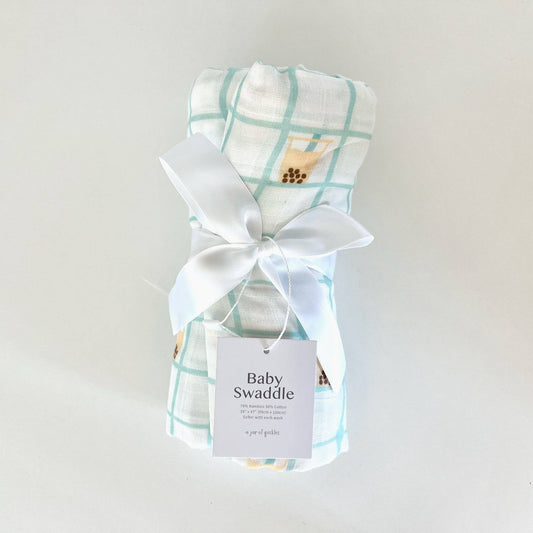 Baby swaddle with plaid pattern and cartoon design, tied with a white ribbon on a light gray background.