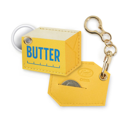 A yellow faux-leather keychain wallet shaped like a butter carton and a matching hexagonal tag, both attached to gold-tone hardware and a white key ring, on a white background.