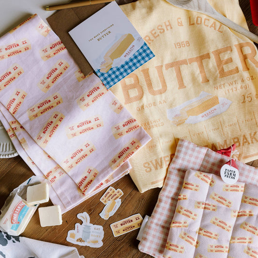 Butter tea towel shown with other butter themed items - shirt, stickers, card.