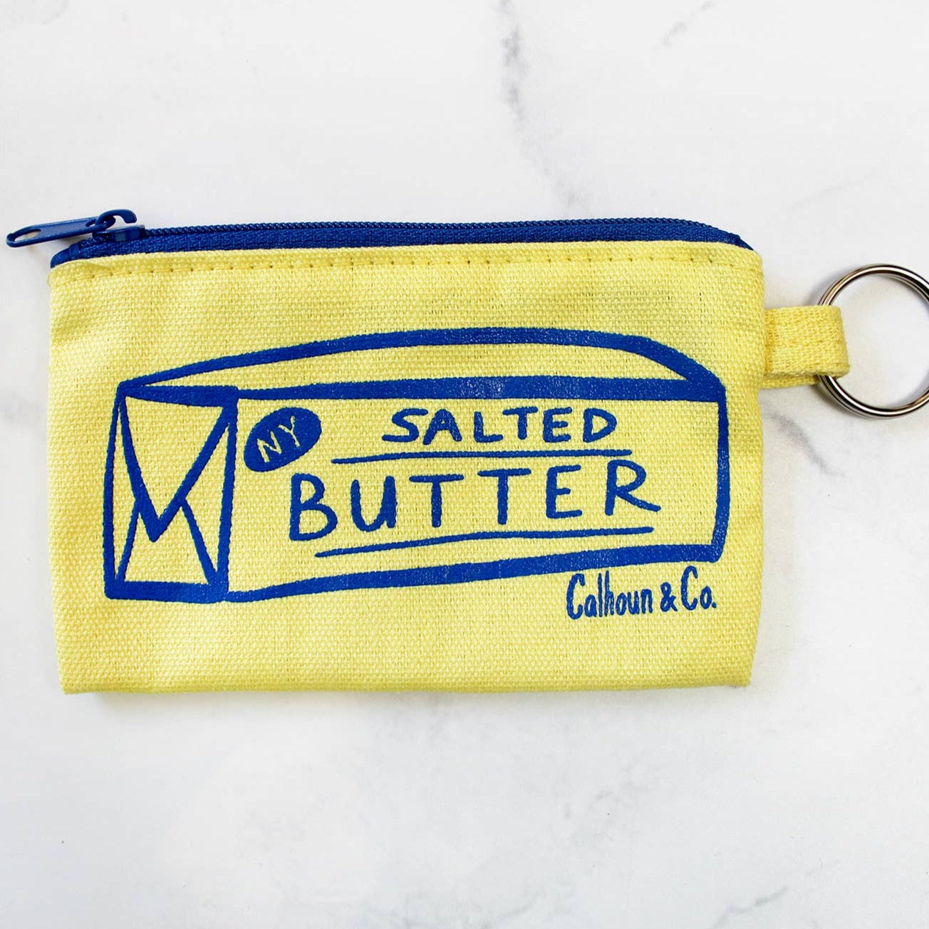 light yellow coin/card purse with a blue zipper, stick of butter printed in blue ink on front. Includes attached keyring 