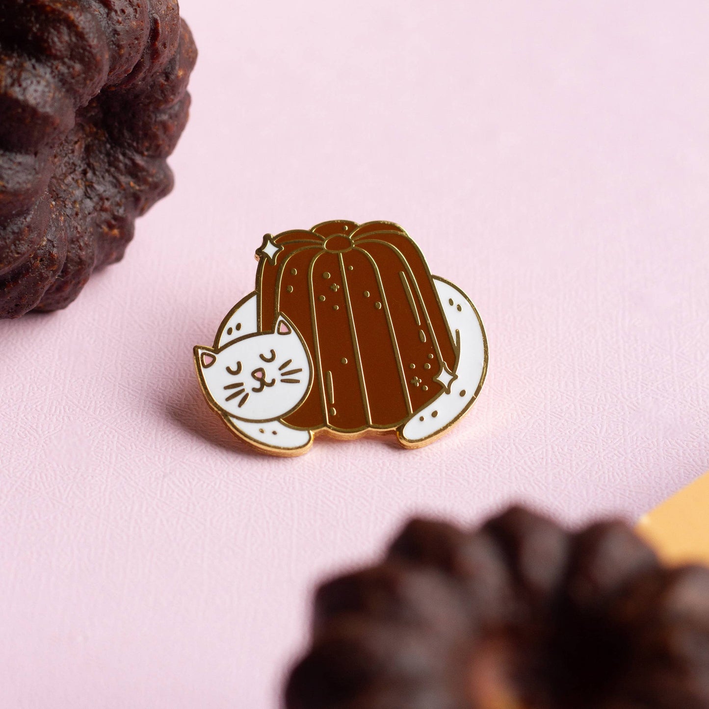 White cat sleeping while hugging a canele pastry. Lapel pin. 