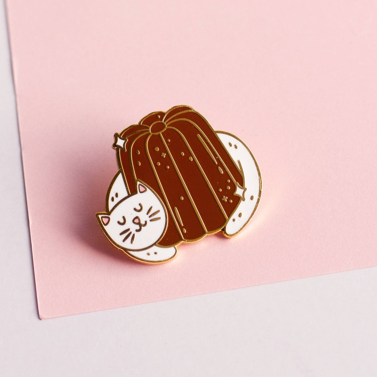 Pink paper background. Cat hugging a canele lapel pin.