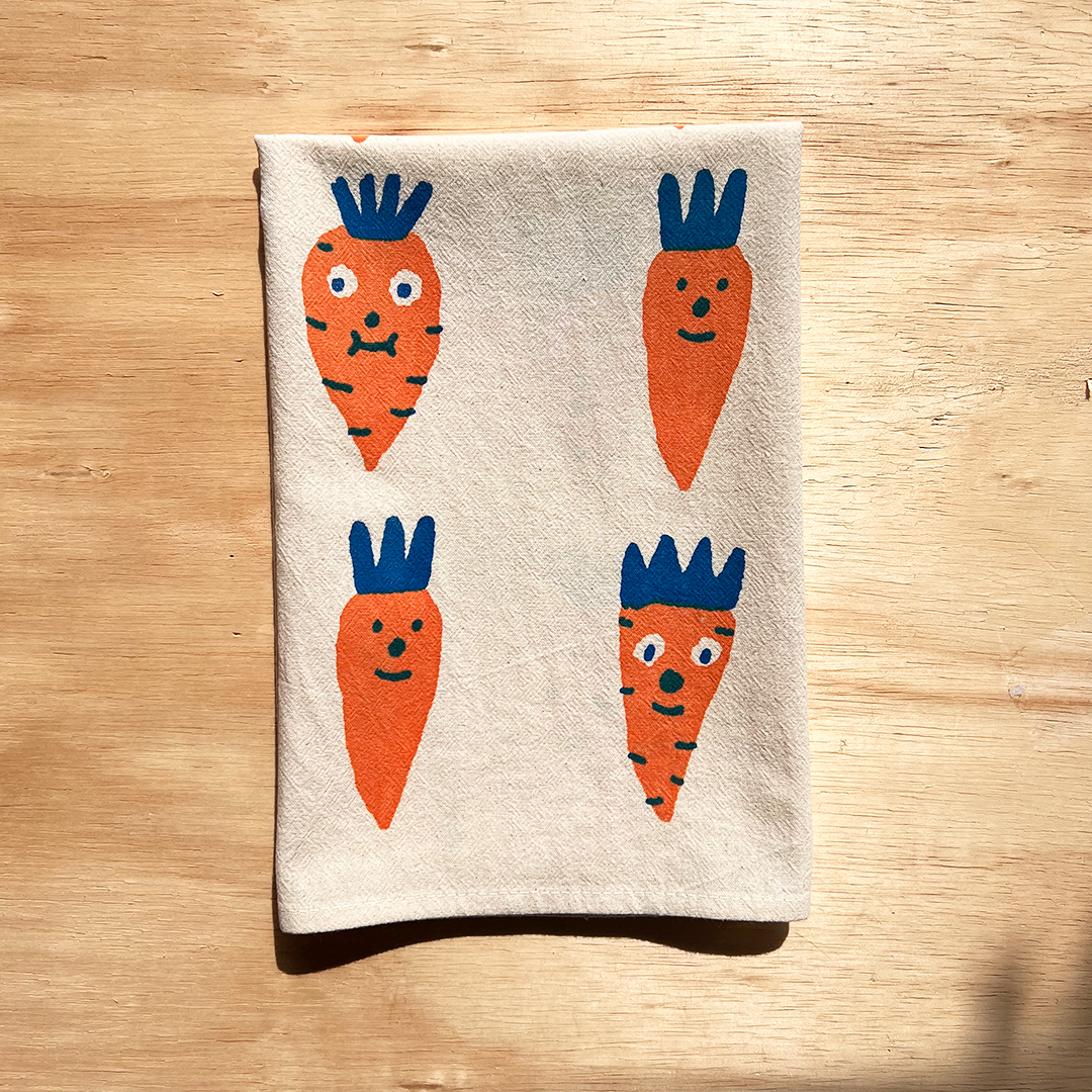 Folded kitchen towel with carrot designs on a wooden surface