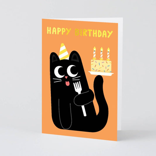 Card with "Happy Birthday" in gold foil and illustration of a black kitty wearing a yellow striped party hat while licking a fork and balancing a birthday cake (with sprinkles and three candles) on its tail.