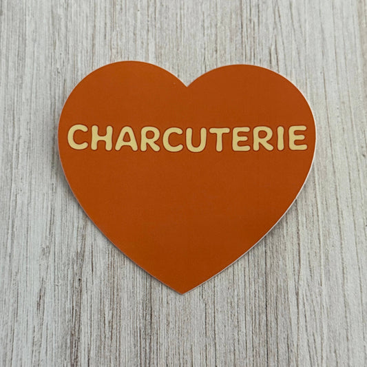 Heart-shaped sign with 'CHARCUTERIE' text on a wooden surface