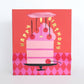 Gift bag with a pink birthday cake design on a red background