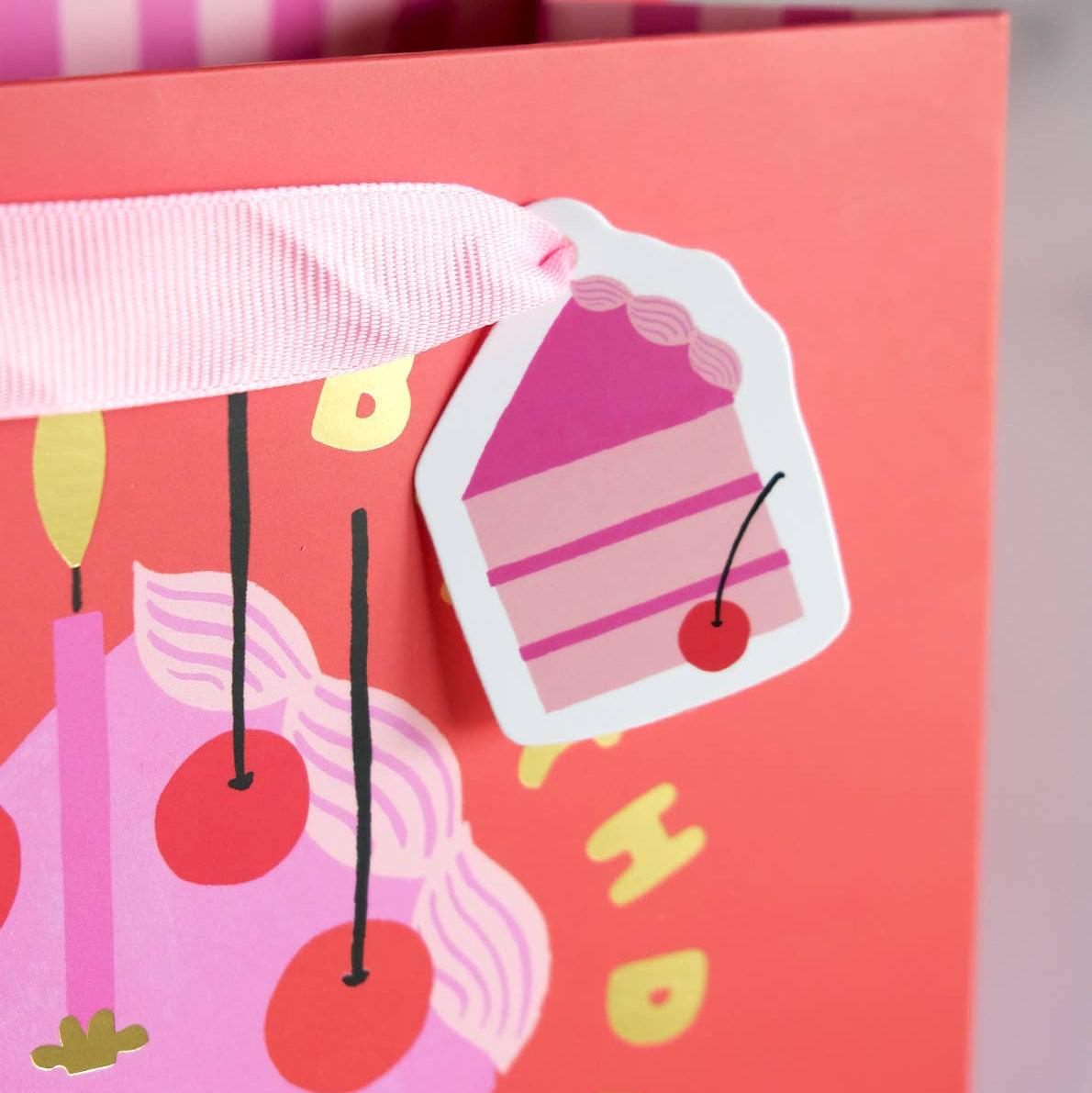 Gift bag with cake design and cherry on top, featuring a pink ribbon.