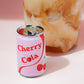 Refillable lighter shaped like a "Cherry Cola" soda can - white with red stripe and pair of cherries on the side. Shown next to a bubbly soda in a glass.
