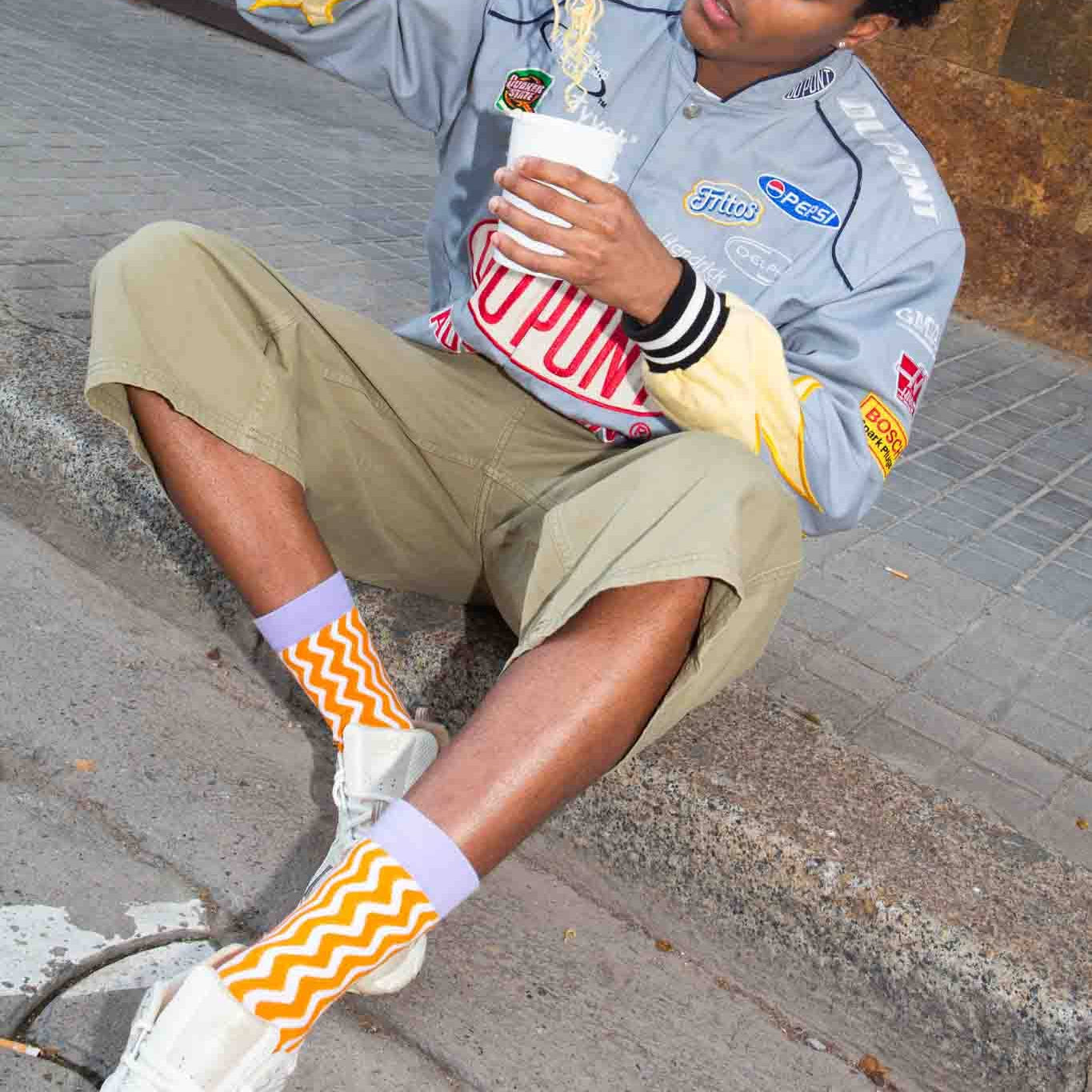 Person sitting on a street curb eating noodles with a casual demeanor