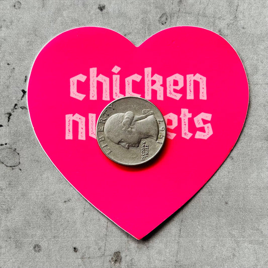 pink, heart shaped sticker with text that reads "chicken nuggets on it" with a quarter on top of it for scale 