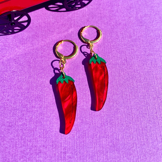 Red chili pepper earrings on a purple surface with a red toy truck in the background.