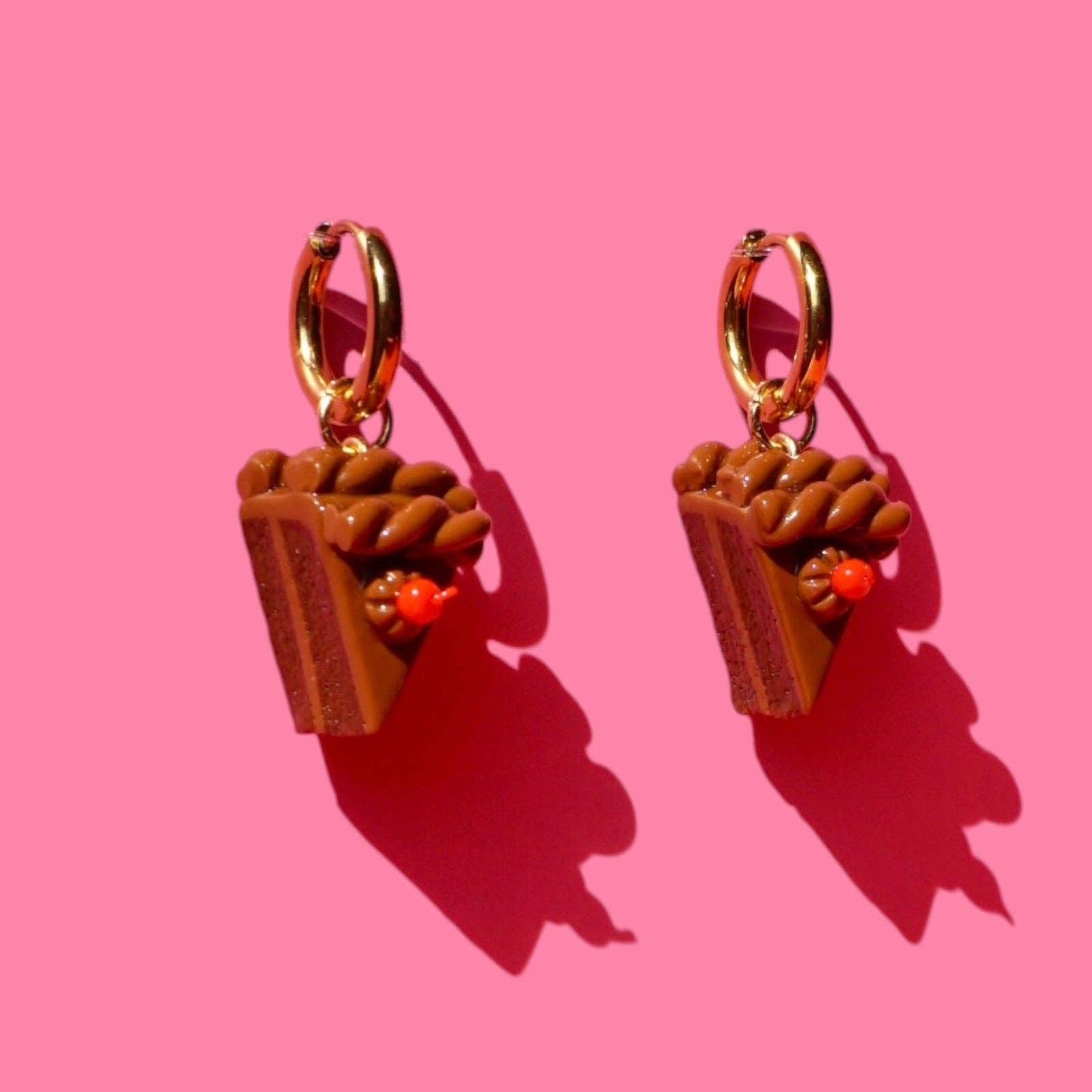 Pair of earrings shaped like small slices of chocolate cake on a pink background