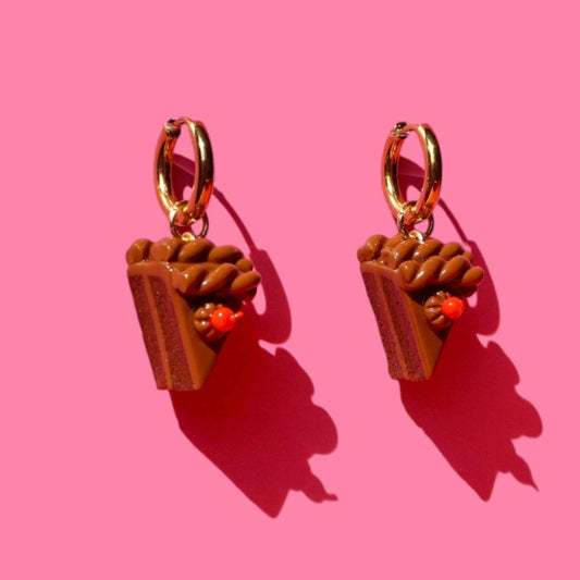 Pair of earrings shaped like small slices of chocolate cake on a pink background