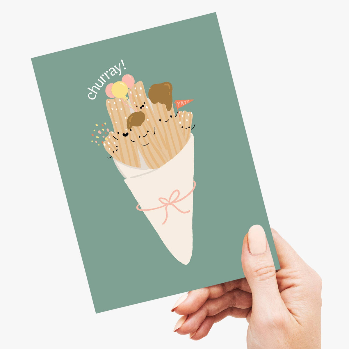 A hand holding a greeting card with a humorous illustration of churros bundled in a cone with faces, and the text 'churray!' on a light gray background.