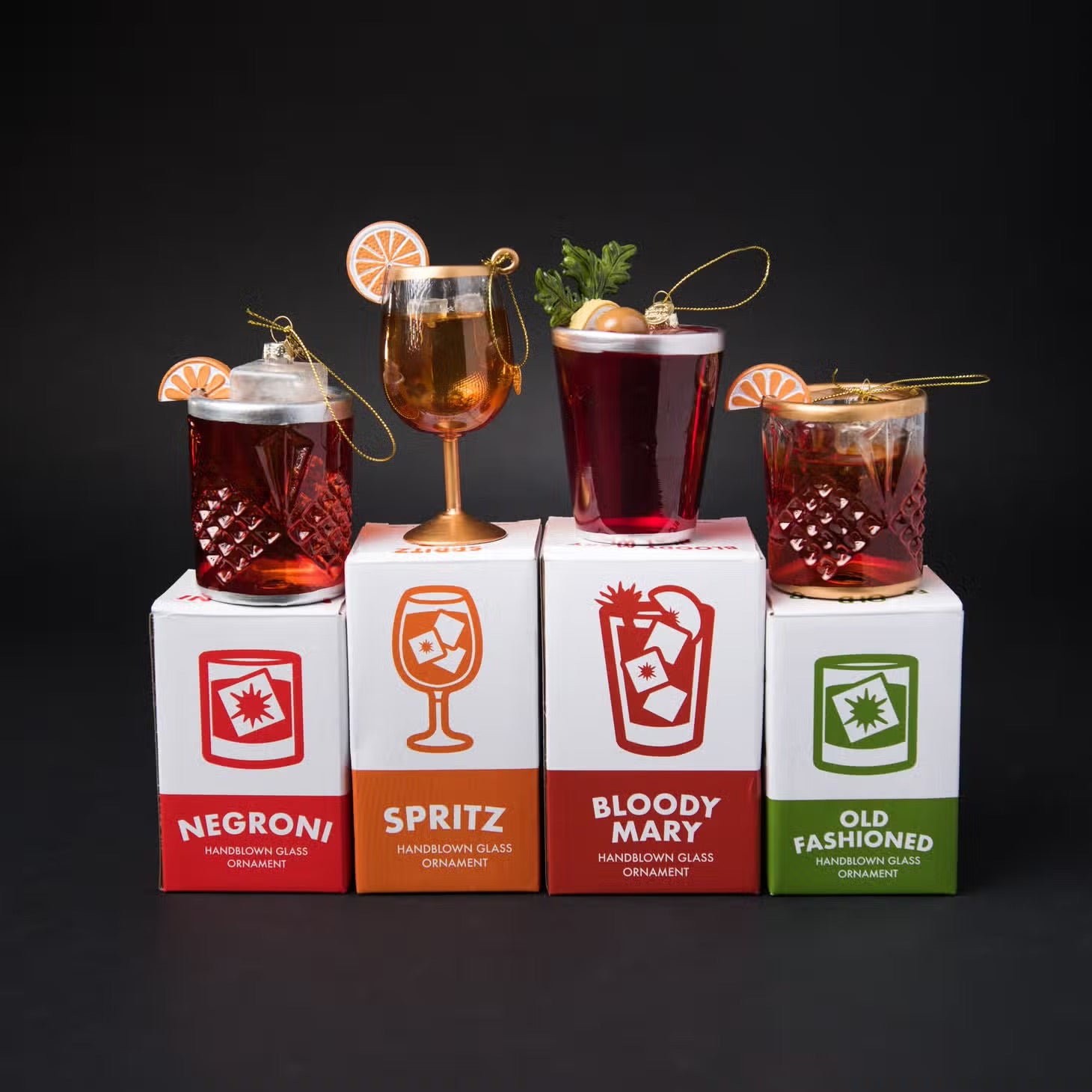 Hand blown glass ornaments on display boxes: Negroni, Spritz, Bloody Mary and Old Fashioned.